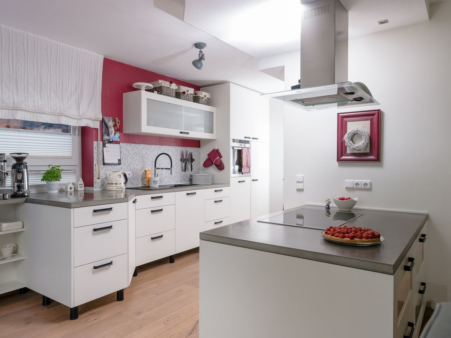 Kücheneinrichtung mit weißen Schränken, roter Akzentwand und zentraler Insel