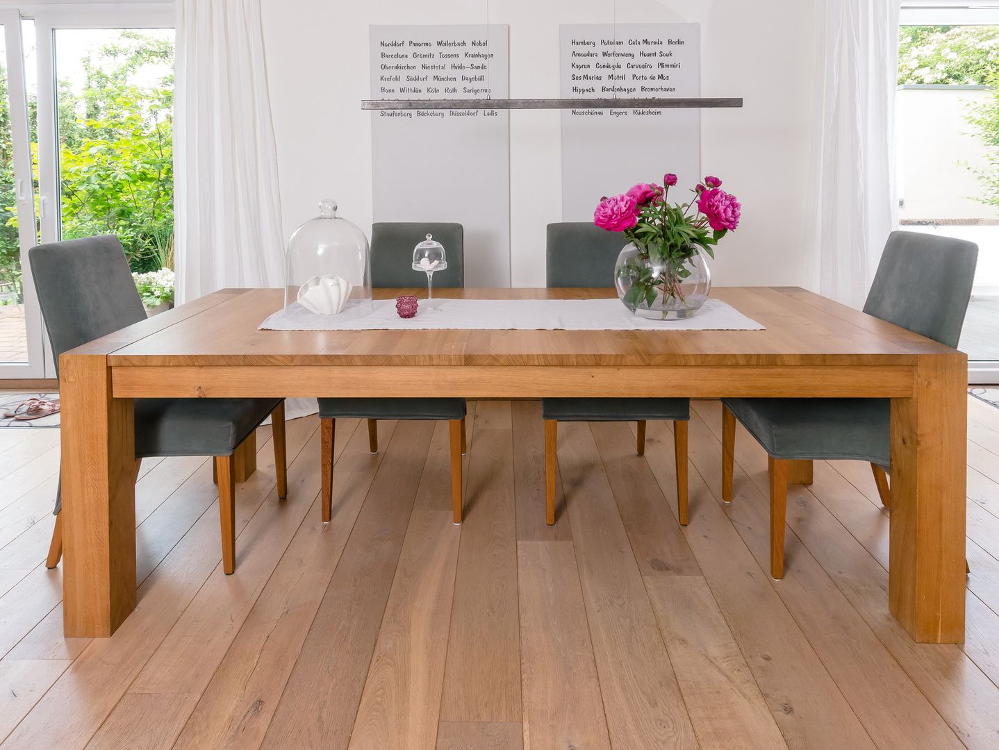 Modernes Esszimmer mit einem Holztisch, grauen Stühlen und einem Strauß rosa Blumen