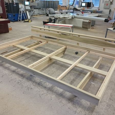 Holzrahmen auf Werkstattboden mit Werkzeugen und Maschinen im Hintergrund