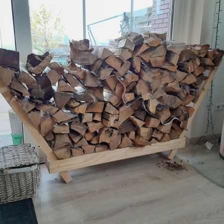 Mit Brennholz gefülltes Holzregal neben einem Ofen