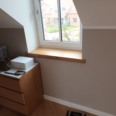 Ein helles Zimmer mit hölzerner Kommode und Fensterregal