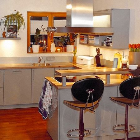 Moderne Küche mit Arbeitsflächen aus Holz, Sitzgelegenheiten an einer Theke und warmer Beleuchtung