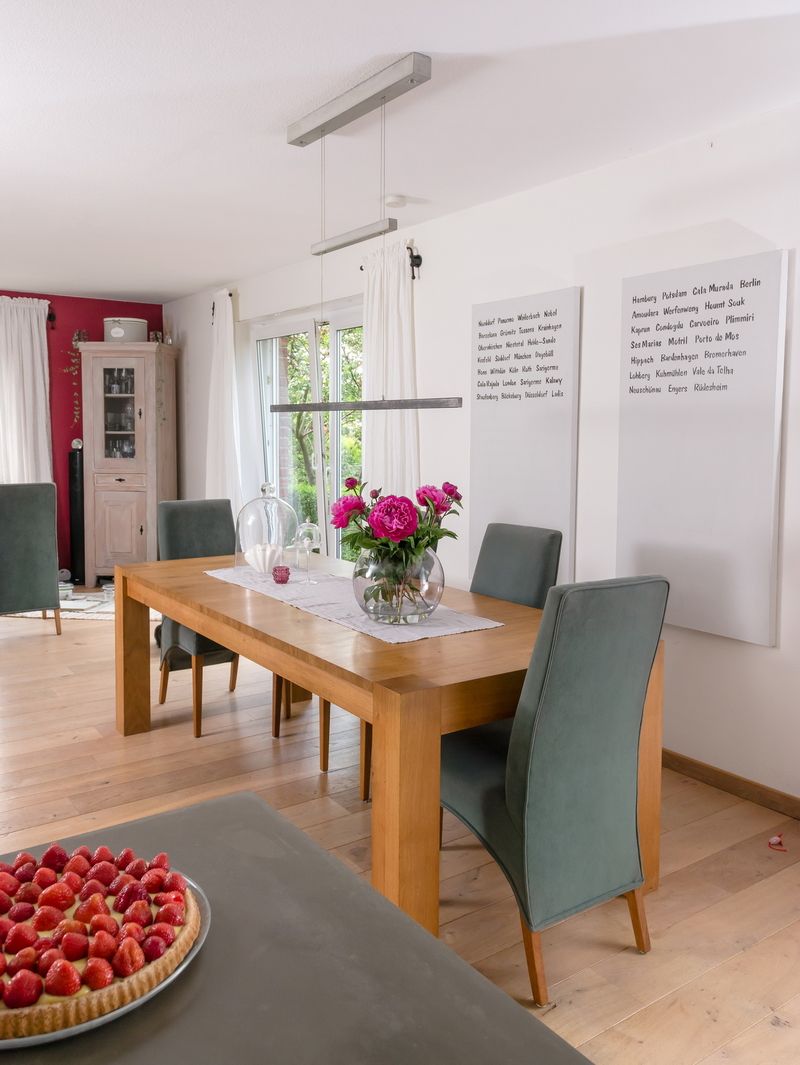 Modernes Esszimmer mit Holztisch, rosa Blumen in einer Vase und Textkunst an der Wand
